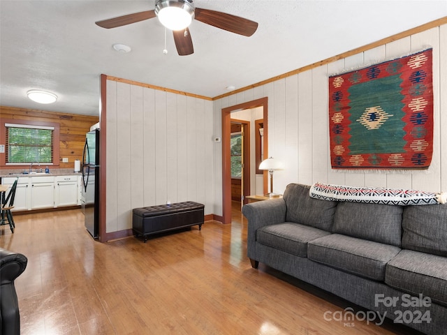 living room with a textured ceiling, wood walls, light hardwood / wood-style floors, sink, and ceiling fan