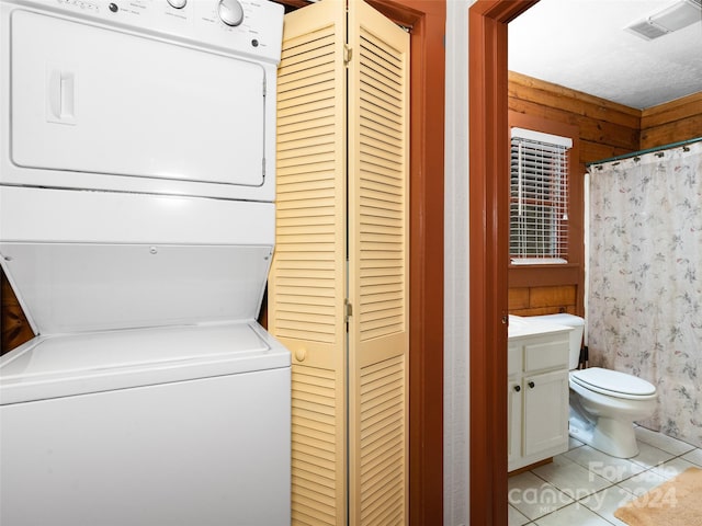 laundry area featuring a textured ceiling, stacked washer and clothes dryer, and light tile patterned flooring