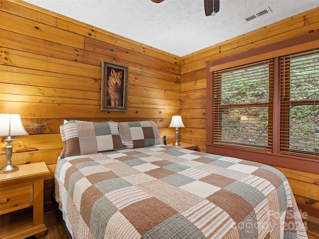 bedroom with a textured ceiling, ceiling fan, hardwood / wood-style floors, and wooden walls