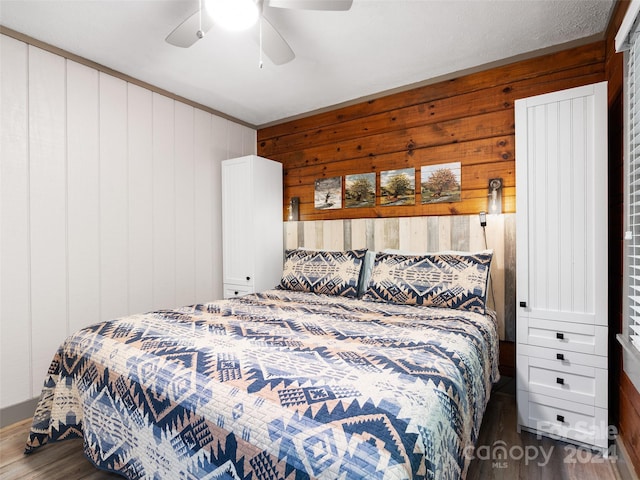 bedroom featuring dark wood-type flooring, ceiling fan, and wooden walls