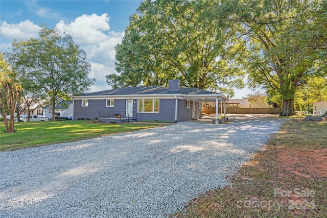 ranch-style house with a chimney, a front lawn, driveway, a carport, and fence