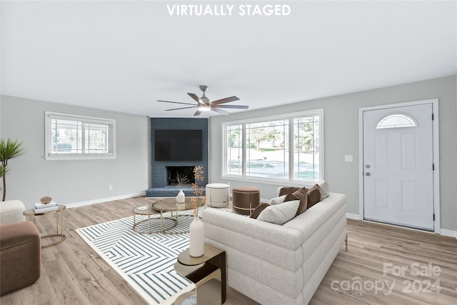 living room featuring light wood-style floors, a brick fireplace, baseboards, and ceiling fan