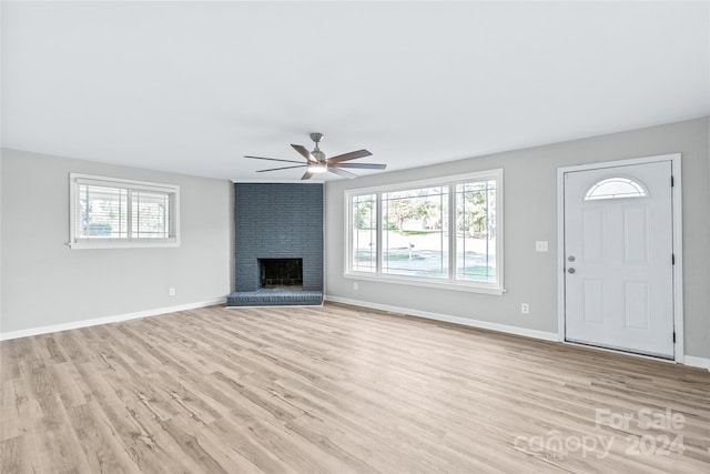 unfurnished living room featuring baseboards, a ceiling fan, a brick fireplace, and light wood-style floors