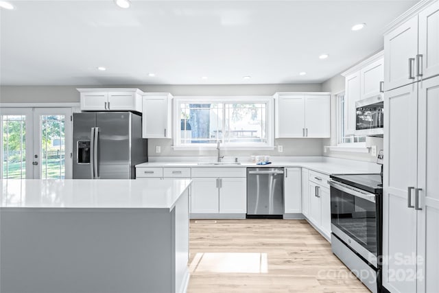 kitchen with appliances with stainless steel finishes, white cabinets, a healthy amount of sunlight, and light wood-type flooring