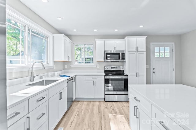 kitchen with a wealth of natural light, appliances with stainless steel finishes, white cabinetry, and a sink