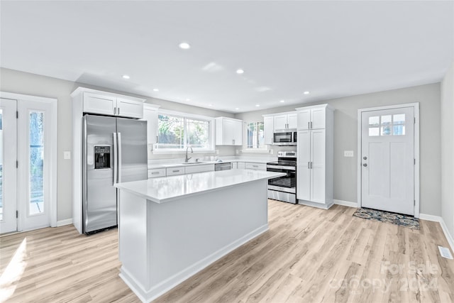 kitchen featuring appliances with stainless steel finishes, sink, light wood-type flooring, a center island, and white cabinetry