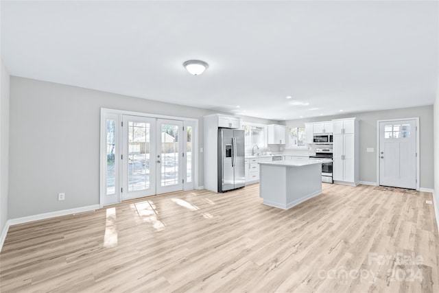 kitchen with appliances with stainless steel finishes, white cabinetry, light hardwood / wood-style flooring, french doors, and a center island