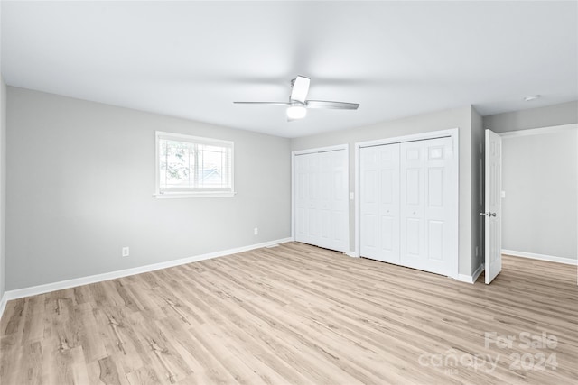 unfurnished bedroom featuring light wood-style floors, multiple closets, baseboards, and ceiling fan