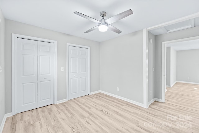 unfurnished bedroom with attic access, baseboards, light wood-style floors, a ceiling fan, and multiple closets
