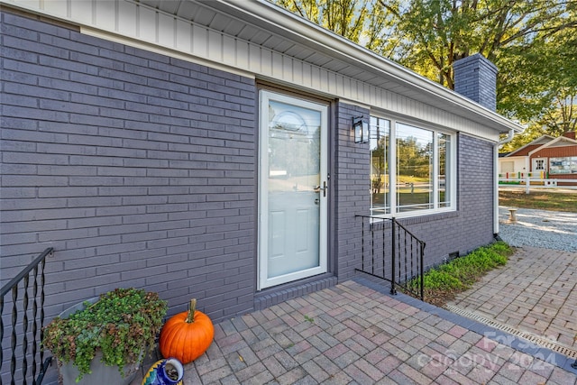 doorway to property with a chimney, brick siding, and a patio