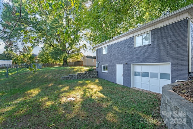 view of home's exterior with fence, a lawn, brick siding, and a garage