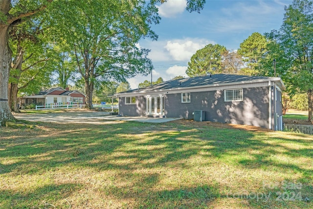 rear view of house with a lawn, brick siding, central AC, and a patio