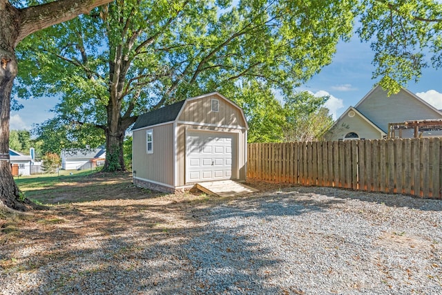 detached garage with fence, driveway, and a storage shed