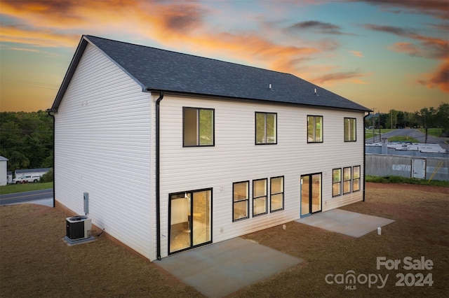 back house at dusk with central AC and a patio area