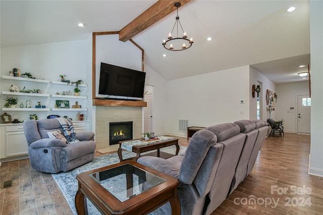 living room with hardwood / wood-style flooring, a tiled fireplace, a chandelier, and vaulted ceiling with beams