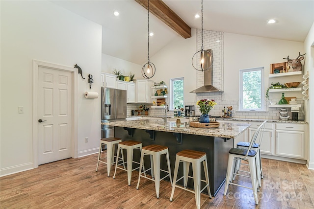 kitchen with light wood-type flooring, light stone counters, white cabinetry, stainless steel refrigerator with ice dispenser, and a kitchen island with sink