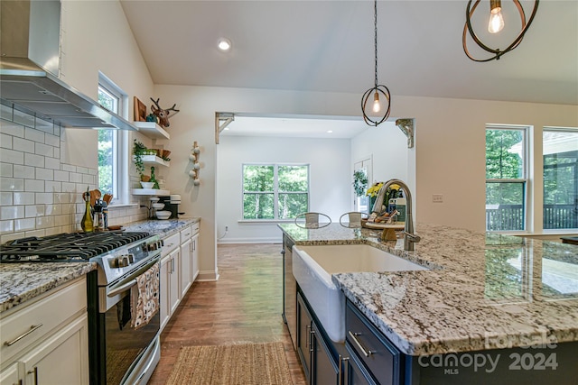 kitchen with white cabinets, stainless steel range with gas cooktop, blue cabinetry, exhaust hood, and a center island with sink