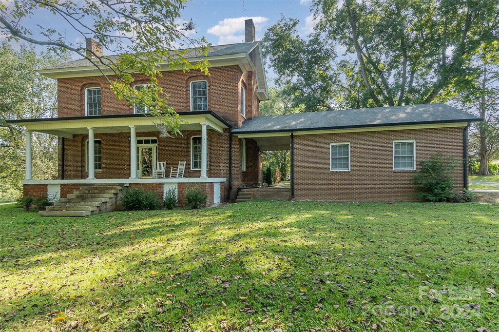 italianate house featuring covered porch, brick siding, and a front yard