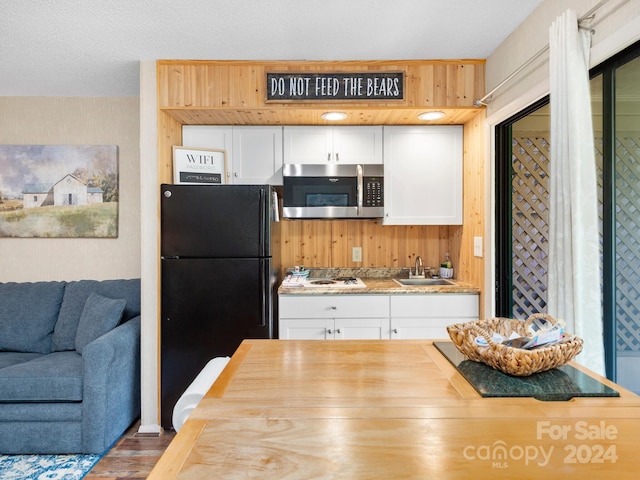 kitchen with sink, hardwood / wood-style floors, black fridge, and white cabinetry