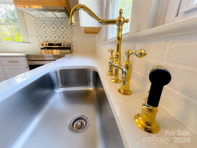 room details featuring custom exhaust hood, backsplash, stainless steel electric stove, and white cabinetry