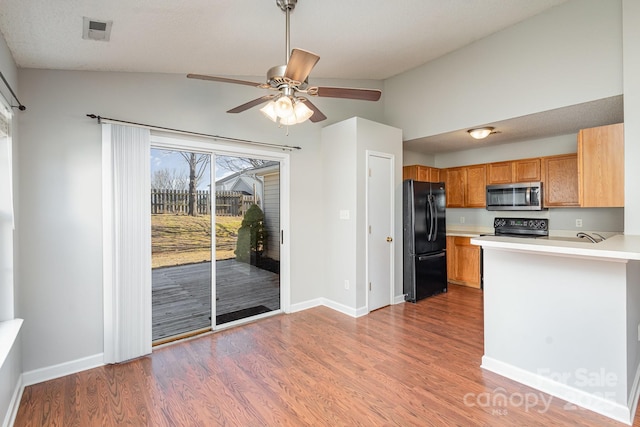 kitchen featuring range with electric stovetop, vaulted ceiling, black refrigerator, hardwood / wood-style floors, and kitchen peninsula