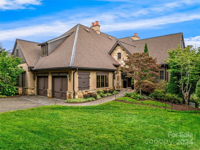 22 Foxbridge Way, Arden, NC 28704 - view of front of home with stone siding, driveway, a front lawn, a chimney, and an attached garage