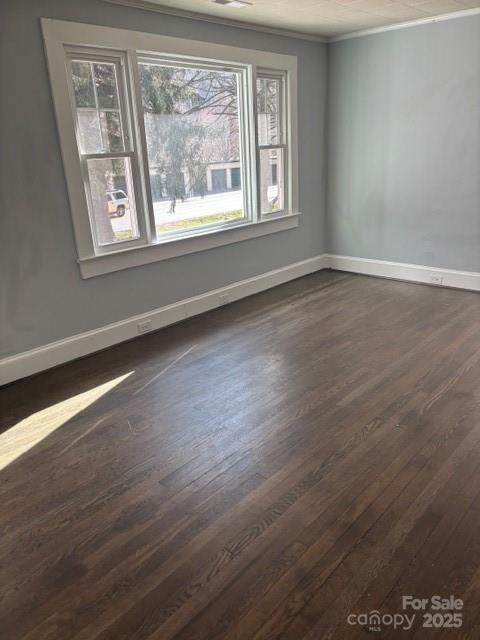 unfurnished room with dark wood-type flooring, crown molding, and baseboards