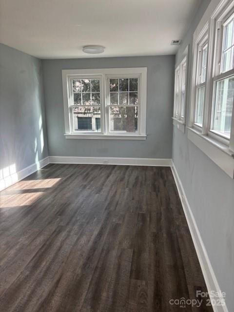 spare room with a healthy amount of sunlight, dark wood-type flooring, visible vents, and baseboards