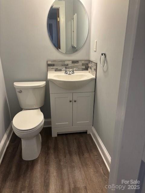 half bath with baseboards, decorative backsplash, toilet, wood finished floors, and vanity