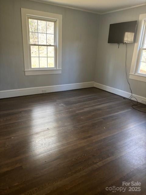 spare room with dark wood finished floors, crown molding, and baseboards