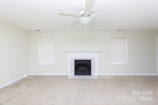 unfurnished living room featuring a textured ceiling, ceiling fan, a tiled fireplace, and light carpet