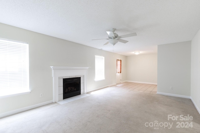 unfurnished living room featuring a textured ceiling, ceiling fan, a tiled fireplace, and light carpet