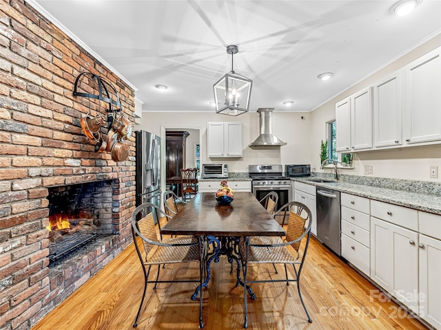 kitchen with white cabinetry, appliances with stainless steel finishes, hanging light fixtures, wall chimney exhaust hood, and light stone counters