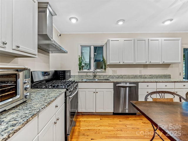 kitchen featuring stainless steel appliances, light wood-type flooring, wall chimney range hood, white cabinets, and sink