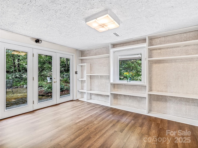 unfurnished living room with a textured ceiling, hardwood / wood-style flooring, and french doors