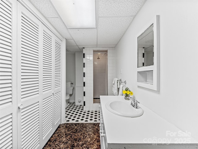 bathroom with walk in shower, vanity, a drop ceiling, and toilet