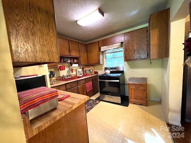 kitchen featuring butcher block countertops, a textured ceiling, stainless steel range, and exhaust hood