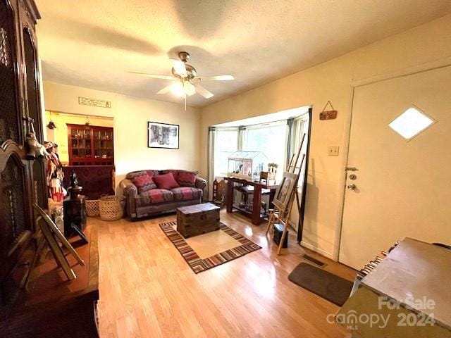 living room with a textured ceiling, ceiling fan, and hardwood / wood-style flooring