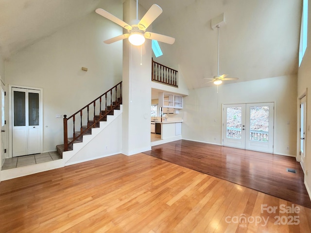 unfurnished living room featuring ceiling fan, high vaulted ceiling, light hardwood / wood-style floors, and french doors