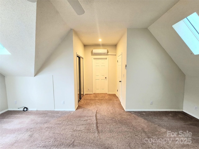 bonus room with lofted ceiling with skylight, a wall mounted air conditioner, carpet, ceiling fan, and a textured ceiling