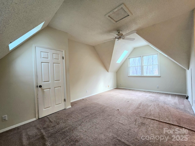 additional living space featuring ceiling fan, carpet flooring, vaulted ceiling with skylight, and a textured ceiling