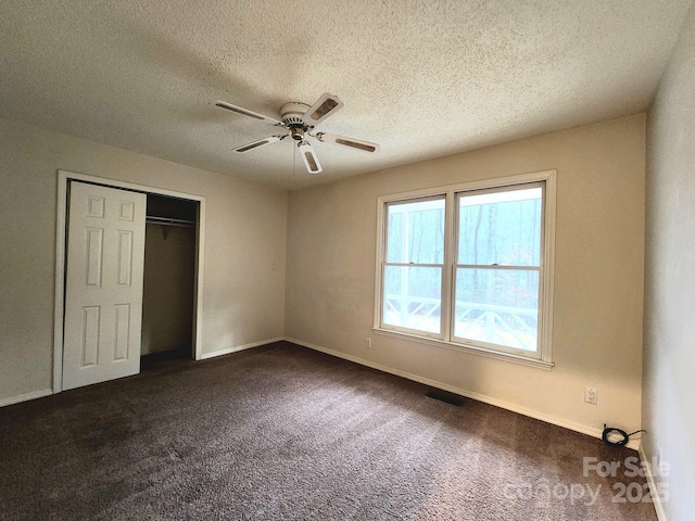 unfurnished bedroom featuring dark colored carpet, ceiling fan, a textured ceiling, and a closet