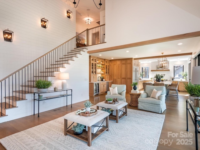 living room with a high ceiling, hardwood / wood-style floors, beverage cooler, and an inviting chandelier