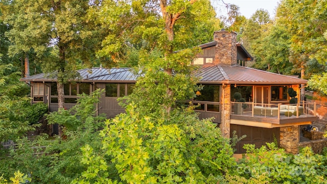 back of house featuring a balcony, a chimney, a standing seam roof, metal roof, and stone siding