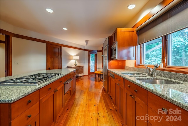 kitchen with a sink, stainless steel appliances, brown cabinetry, light wood-type flooring, and a warming drawer