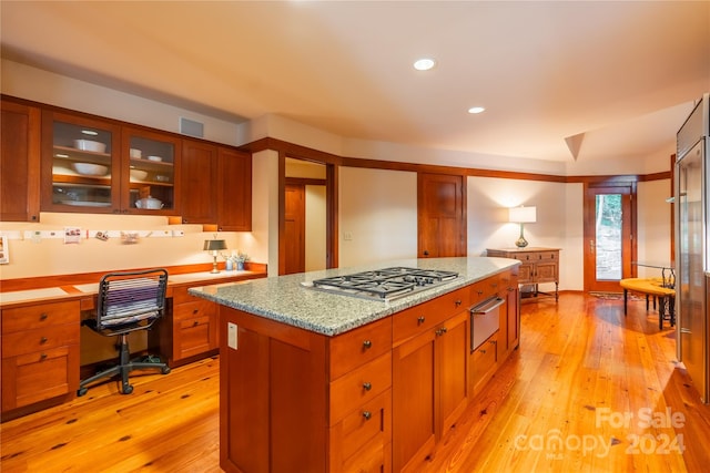 kitchen featuring built in desk, light stone countertops, stainless steel gas stovetop, light hardwood / wood-style flooring, and a center island