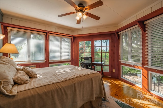 bedroom featuring wood walls, wood-type flooring, multiple windows, and ceiling fan