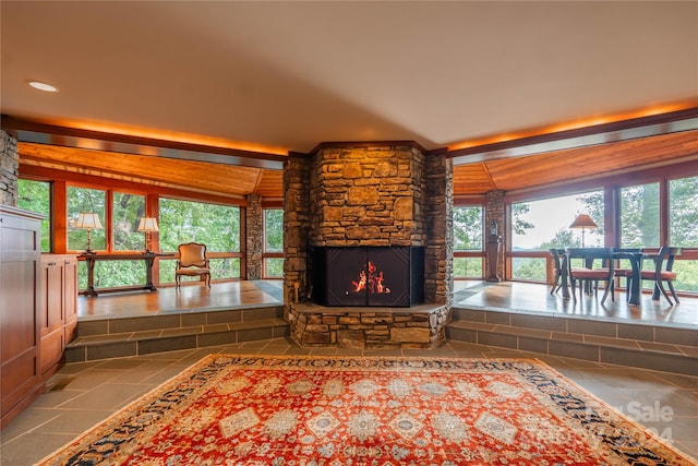 unfurnished living room with a stone fireplace, vaulted ceiling with beams, and a healthy amount of sunlight