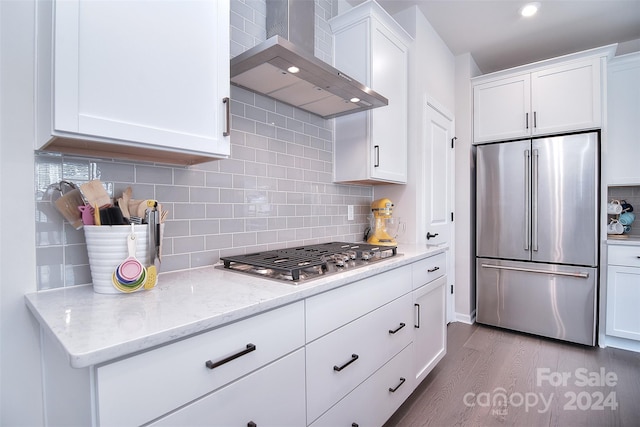 kitchen with wall chimney exhaust hood, stainless steel appliances, white cabinetry, and light hardwood / wood-style floors