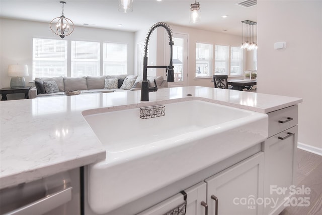 interior details featuring sink, white cabinets, light stone counters, and decorative light fixtures